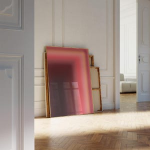 以下が含まれることがあります： ピンク、オレンジ、イエローのグラデーションで描かれた大きな抽象画。絵画は薄い金のフレームで額装され、白い壁に立てかけられている。
