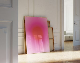 Puede incluir: Una obra de arte enmarcada con un degradado rosa y naranja, con un marco dorado, apoyada contra una pared blanca en una habitación con suelo de madera.