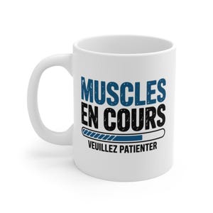 Peut inclure: Mug en céramique blanche avec une anse incurvée. Le mug présente le texte "MUSCLES EN COURS" en bleu et noir, avec un graphique de barre de chargement et le texte "VEUILLEZ PATIENTER" en dessous. Design humoristique sur le thème du fitness.