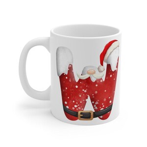 Peut inclure: Mug en céramique blanche avec la lettre "W" rouge décorée sur le thème du Père Noël. La lettre a une ceinture noire, des flocons de neige blancs et un bonnet de Père Noël. Une tasse sur le thème des fêtes.