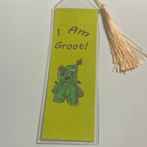 Può includere: Un segnalibro verde e giallo con un disegno di un personaggio verde con il testo "I Am Groot!" su di esso.