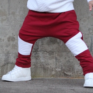May include: Red and white sweatpants with a unique design. The pants have a white stripe down the side of each leg.