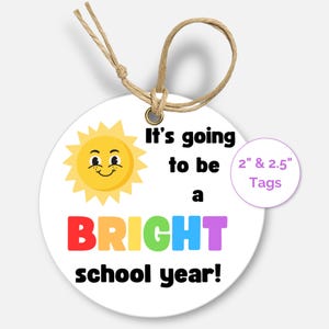 May include: Round tag with a smiling sun and the text "It's going to be a BRIGHT school year!" in rainbow colors. The tag is 2 inches and 2.5 inches in diameter.