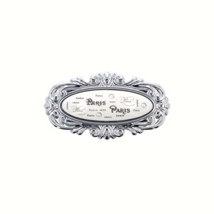 May include: An oval, silver-coloured decorative piece with the word "Paris" in different fonts. The item has a detailed, scrolling border and a white central panel with the word "Paris" repeated. The design is ornate.