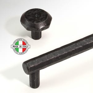 Peut inclure: Poignée et bouton de meuble en métal noir avec une finition martelée. La poignée est de forme rectangulaire allongée avec une légère courbe à l'extrémité. Le bouton est rond avec un dessus plat. La quincaillerie est fabriquée en Italie.