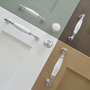 May include: A collection of cabinet hardware featuring white ceramic handles with polished chrome ends and matching round knobs. One knob displays the text "FARM MARKET 1890" in black print. The hardware is mounted on various colored cabinet doors.
