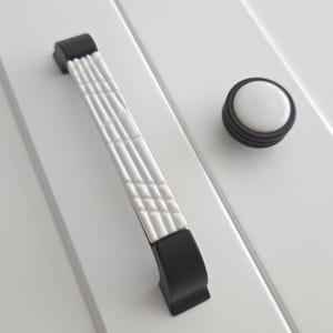 May include: White ceramic cabinet knob with black trim and a matching black and white cabinet pull with a textured design.