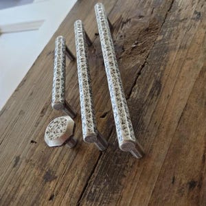 May include: A set of three silver-toned metal cabinet pulls and one matching hexagonal cabinet knob. Each piece features a textured, speckled finish with a dark gray and silver appearance. The hardware has a cylindrical bar design with rounded ends.