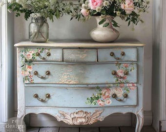 May include: A distressed, light blue chest of drawers with floral decals and ornate hardware. The chest has five drawers and a carved floral design on the apron. The top is cream-colored, and the chest is adorned with bouquets of flowers.