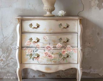 Könnte beinhalten: Eine Kommode mit drei Schubladen in abgenutzter Cremefarbe, verziert mit goldenen Metallgriffen und einem Rosenmuster auf den unteren beiden Schubladen. Der Text re-design with prima #674632 blush symphony ist sichtbar.