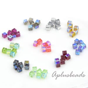 May include: A collection of small, multi-colored cube-shaped beads arranged in clusters. The beads feature iridescent finishes in shades of pink, blue, green, yellow, and silver. The text Aplusbeads is printed in the bottom right corner.
