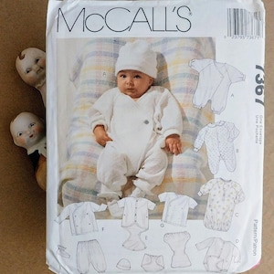 May include: A McCall's sewing pattern envelope labeled 7367 featuring a photograph of an infant wearing a white long-sleeved wrap-style romper and a matching beanie. The envelope displays various technical line drawings of baby clothing designs.