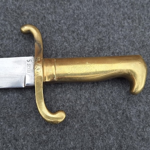 Könnte beinhalten: Ein Schwert mit einer polierten, silberfarbenen Metallklinge und einem massiven Messinggriff. Das Parierstange ist geschwungen gestaltet und die Klinge ist nahe dem Heft mit der Zahl 5 gestempelt. Der Griff hat eine glatte Form und einen Knauf.
