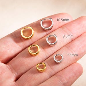 May include: A collection of six small hoop earrings in gold and silver tones, arranged in pairs of varying sizes. The labels indicate diameters of 10.5mm, 9.5mm, and 7.5mm for the respective pairs, showcasing a simple, circular metal design.