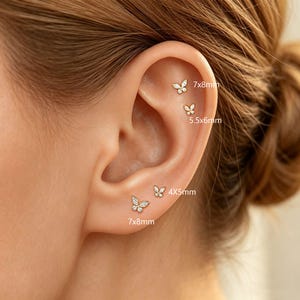 May include: Four gold butterfly-shaped stud earrings with clear stones, featuring sizes labeled as 7x8mm, 5.5x6mm, 4x5mm, and 7x8mm. The earrings are arranged along the ear cartilage and lobe, showcasing a delicate metallic design with sparkling accents.