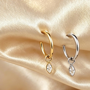 Peut inclure: Deux boucles d'oreilles créoles, l'une en ton doré poli et l'autre en ton argenté poli, chacune dotée d'une petite breloque en cristal transparent taille marquise suspendue à un anneau circulaire fixé à la base de la créole.