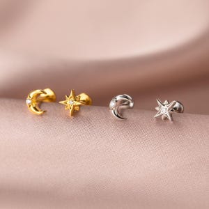May include: Four celestial-themed stud earrings. Two are gold-toned, featuring a crescent moon and a starburst design. The other two are silver-toned, with a crescent moon and a starburst design. All earrings have a small, sparkling accent.