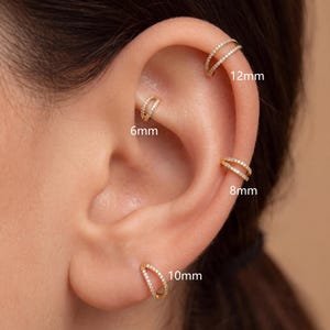 May include: Four gold-toned double-band hoop earrings featuring small clear stones. The earrings are labeled with sizes 6mm, 8mm, 10mm, and 12mm, indicating their respective diameters as they are positioned on different parts of the ear cartilage and lobe.