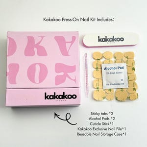 May include: A pink Kakakoo press-on nail kit with a box, nail file, alcohol pads, cuticle stick, and sticky tabs. The box has the brand name and logo in black and pink. The kit includes a reusable nail storage case.