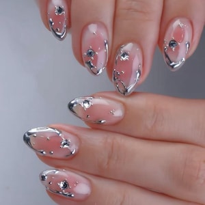May include: Close-up of a set of manicured nails. Each nail features a clear base with a pink gradient and silver metallic accents. Small, sparkling rhinestones are embedded in the design, adding a touch of glamour to the overall look.
