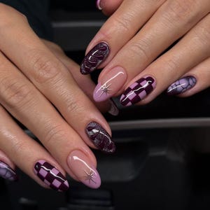 May include: Close-up of manicured nails in various designs. Some nails are a deep burgundy with silver glitter, others are a light pink with a starburst design, and some feature a checkerboard pattern in burgundy and purple.