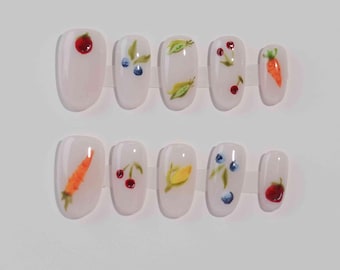 May include: Set of ten false nails with a white base and various painted designs of fruits and vegetables, including cherries, blueberries, corn, carrots, and leaves.