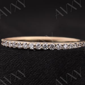 May include: A slender gold ring adorned with small, glittering diamonds. The ring has a thin band and a continuous row of evenly spaced, round-cut diamonds. The ring is set against a dark background.