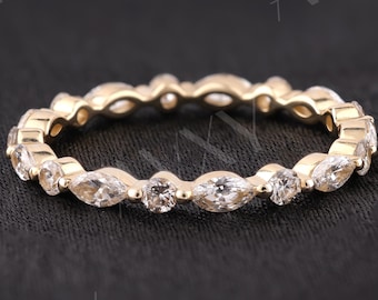 May include: A gold-colored ring with a continuous band of alternating marquise and round-cut clear gemstones. The ring is set against a dark background, highlighting the sparkle of the stones. A delicate piece of jewelry.