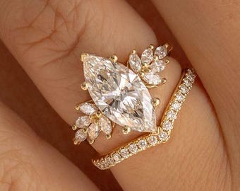 May include: A gold engagement ring featuring a large marquise-shaped diamond surrounded by smaller diamonds. The ring is set on a delicate band with a v-shaped design.