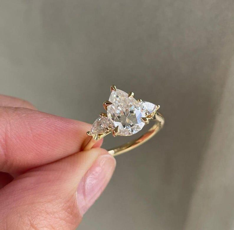 Side profile of a 2 carat lab created pear diamond ring set in a cathedral-style three stone setting. The center pear diamond is flanked by two sparkling stones, creating a meaningful and sustainable engagement ring. A top choice on Etsy for brides looking for ethical diamond jewelry gifts.
