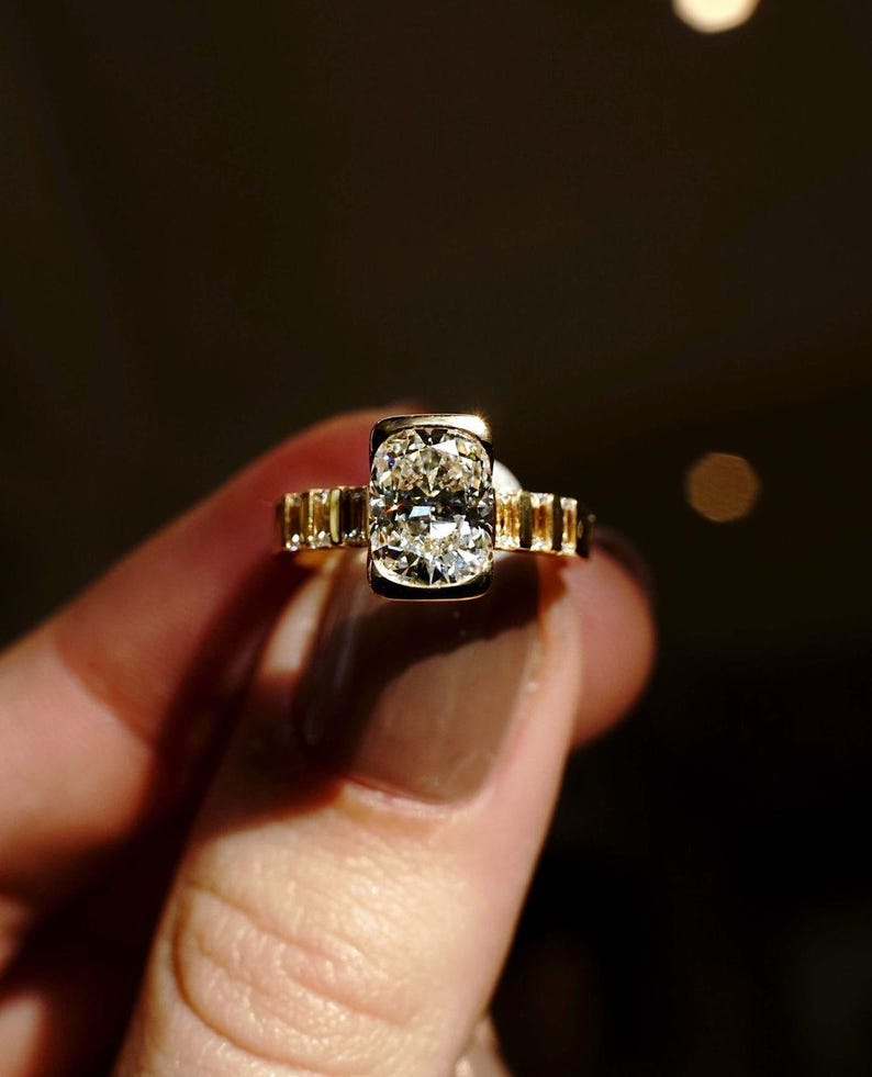 Modern 2ct cushion solitaire lab diamond ring in a half bezel mount with a softly tapered flair shank. Designed as a sustainable engagement or anniversary ring, this elegant piece also makes a perfect gift for her on birthdays or special milestones.