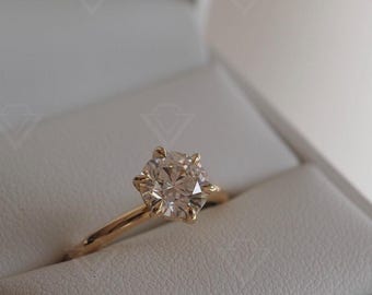 May include: A gold engagement ring with a round, clear diamond in a white box.