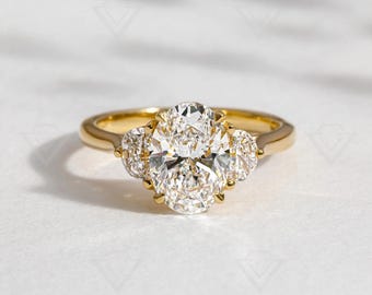 May include: A gold engagement ring featuring a large oval-shaped centre diamond and two smaller pear-shaped diamonds on either side.