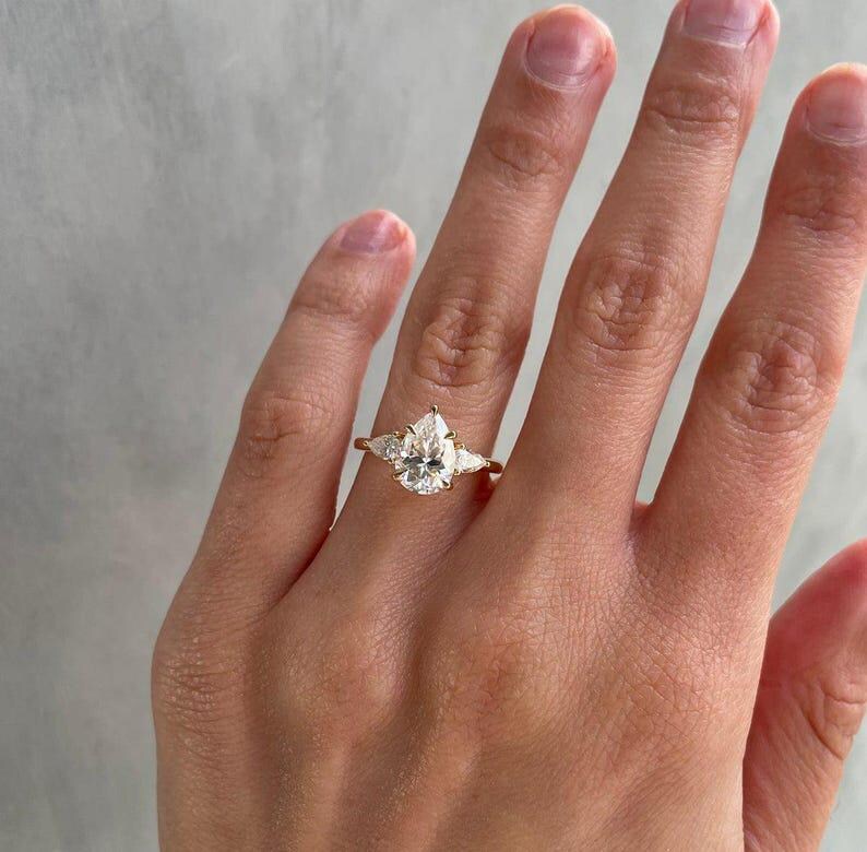 2ct pear-shaped lab grown diamond ring designed with a graceful cathedral setting and accented by two side stones. This three-stone engagement ring symbolizes lasting love and commitment, ideal for anniversaries, proposals, or weddings. Trending among Etsy’s fine lab diamond ring collections.