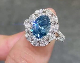 May include: A dazzling silver ring featuring a large, oval-cut, light blue gemstone. The central stone is surrounded by a halo of smaller, clear gemstones, with additional stones adorning the band. The ring is set in a silver metal.