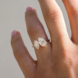 May include: A gold ring with two pear-shaped diamonds set on a band that wraps around the finger.