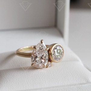 May include: A gold ring with two pear-shaped diamonds and a round diamond. The ring is in a white box.