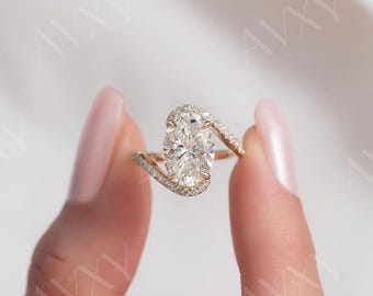 Può includere: Un anello di fidanzamento in oro con una pietra centrale di diamante taglio ovale. L'anello presenta un design unico e a spirale con un alone di diamanti più piccoli attorno alla pietra centrale e lungo la fascia. L'anello è tenuto da una persona.