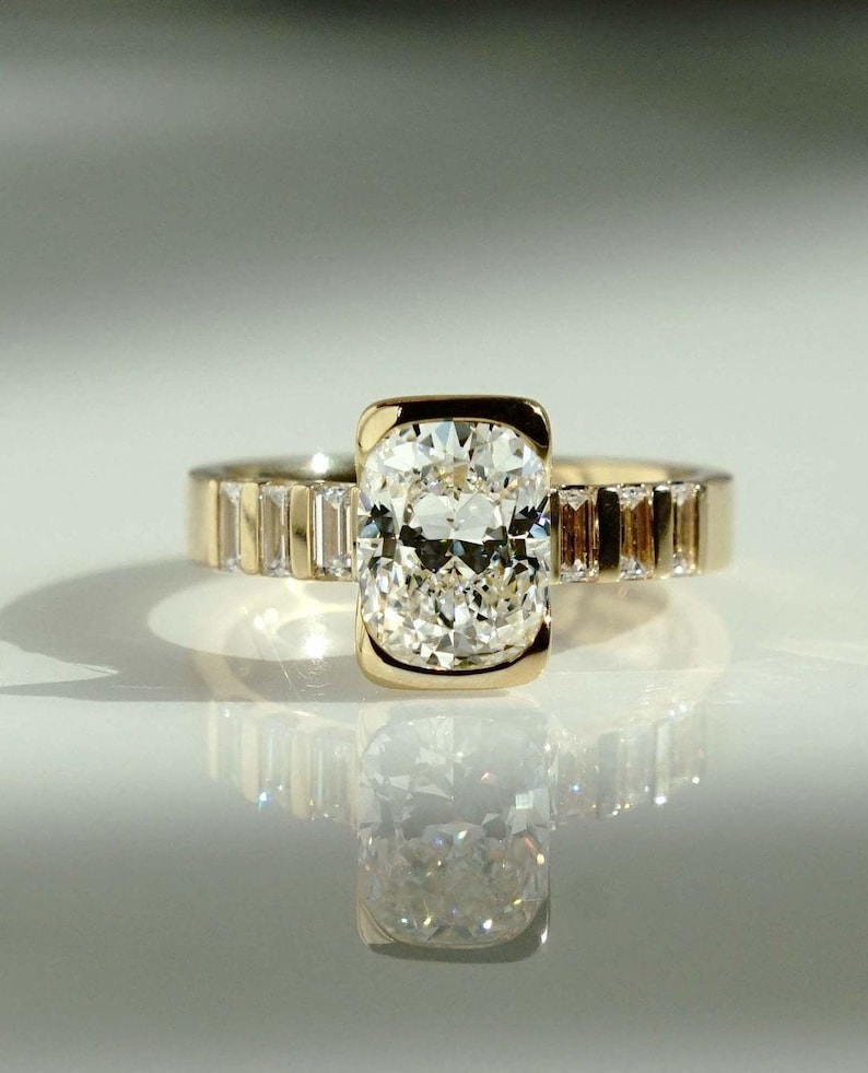 This 2ct cushion cut lab grown diamond solitaire ring features a sleek half bezel setting and a sculpted flair shank for a modern twist. Perfect as an engagement ring, promise ring, or meaningful birthday or anniversary gift for her with ethical sparkle and timeless style.