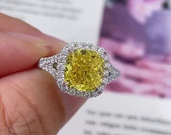May include: A yellow cushion-cut diamond engagement ring with a halo setting and a double band. The ring is set in white gold.
