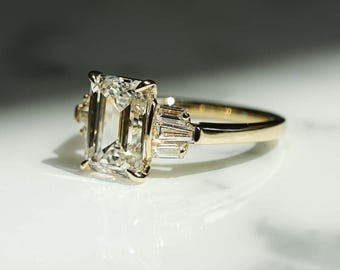 May include: A gold engagement ring with a large, clear emerald-cut diamond and smaller baguette diamonds on the band.