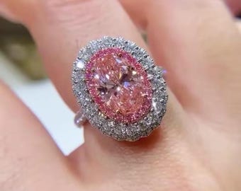 May include: A ring with a large oval pink diamond surrounded by a double halo of smaller diamonds. The ring is set in white gold.