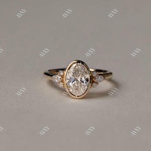 May include: A gold engagement ring with an oval-shaped center diamond and smaller diamonds on the band. The ring is set on a white background.