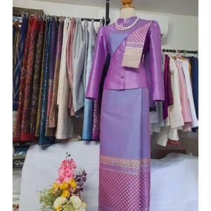 May include: A purple and gold Thai silk dress with a long-sleeved jacket. The dress is on a mannequin and is displayed in a shop.