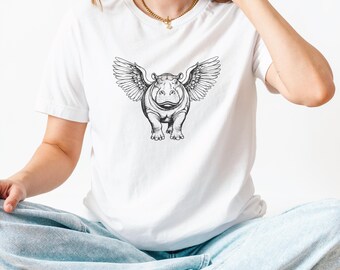 May include: White t-shirt featuring a black and white illustration of a hippopotamus with feathered wings. The graphic is centered on the shirt. The shirt is made of a soft material.