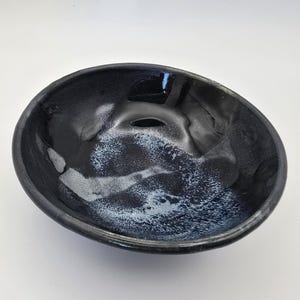 May include: A black ceramic bowl with a white glaze. The glaze has a marbled effect, creating a unique and artistic design.
