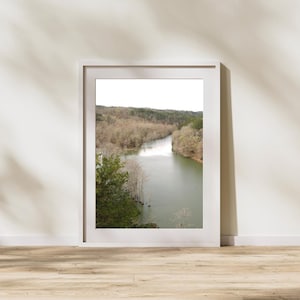 May include: A framed photograph of a river winding through a forest. The river is a light blue-green color and the trees are a mix of brown and green.