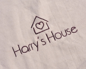 May include: A white fabric tote bag with a brown embroidered logo that says "Harry's House" with a house icon and a heart inside.