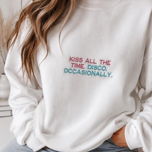 Può includere: Felpa bianca con la scritta ricamata "KISS ALL THE TIME, DISCO, OCCASIONALLY" in rosa e verde acqua. La felpa è a girocollo e a maniche lunghe.