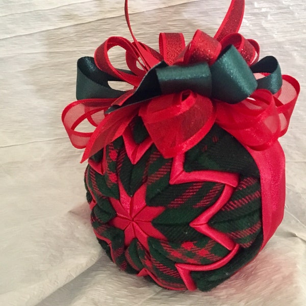 May include: A red and green plaid Christmas ornament with a red and green ribbon bow. The ornament is made of fabric and has a quilted design.